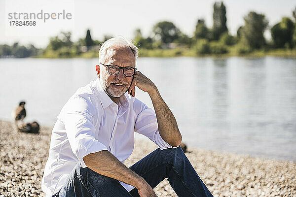Mann sitzt an einem sonnigen Tag am Flussufer