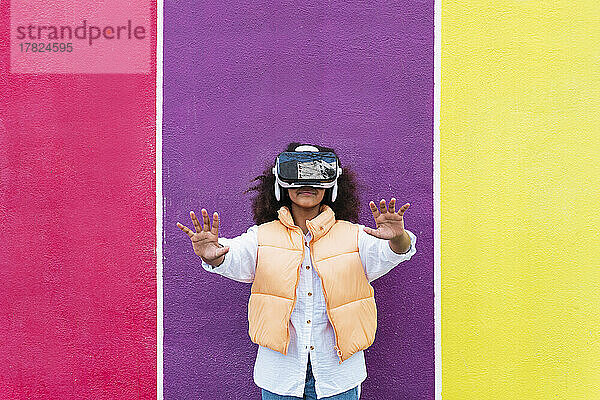 Mädchen mit Virtual-Reality-Simulator gestikuliert vor bunter Wand