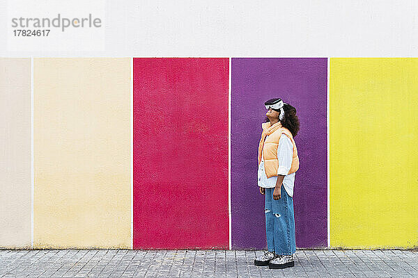 Mädchen trägt Virtual-Reality-Simulator und steht an einer bunten Wand