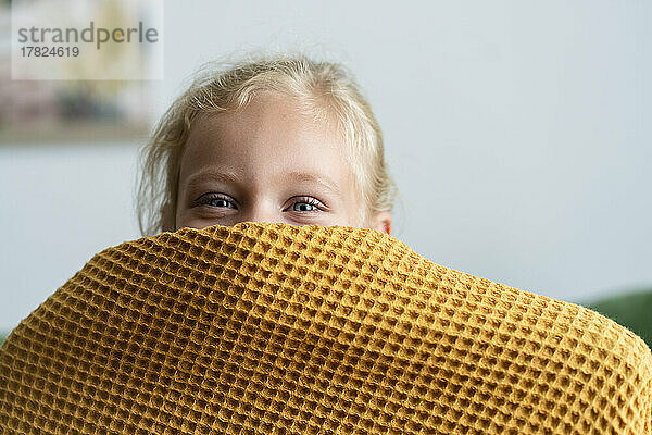 Girl hiding face under blanket at home