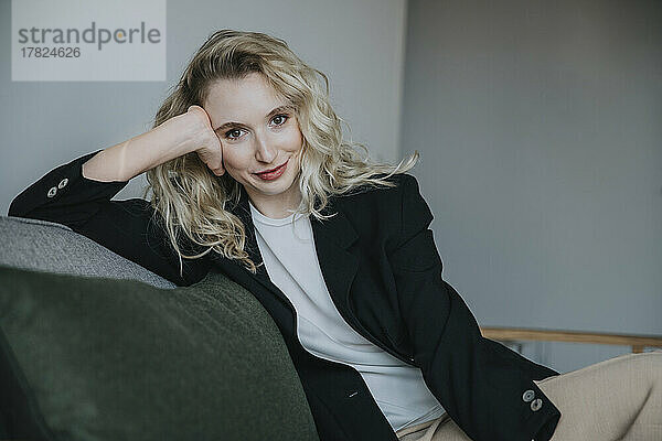 Lächelnde Geschäftsfrau mit blonden Haaren sitzt auf dem Sofa