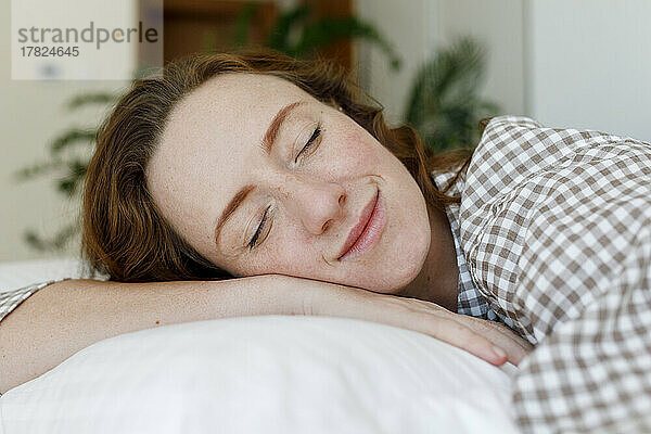 Lächelnde Frau entspannt sich auf einem Kissen im Schlafzimmer
