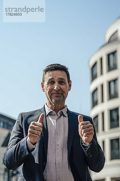 Lächelnder reifer Geschäftsmann zeigt an sonnigem Tag Daumen nach oben