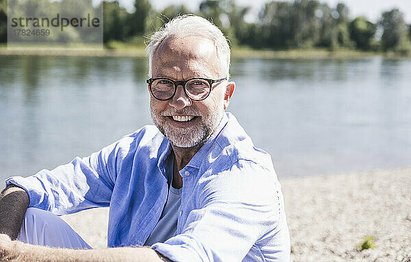 Lächelnder Mann mit Brille am Flussufer an einem sonnigen Tag