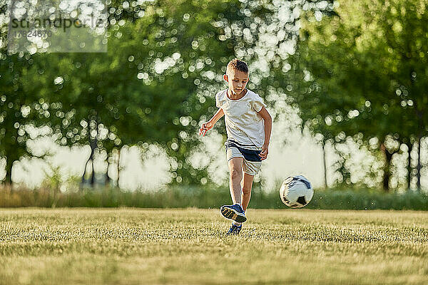 Junge spielt an einem sonnigen Tag Fußball auf dem Sportplatz