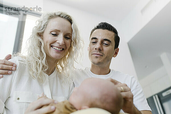 Smiling woman carrying baby sitting by man at home