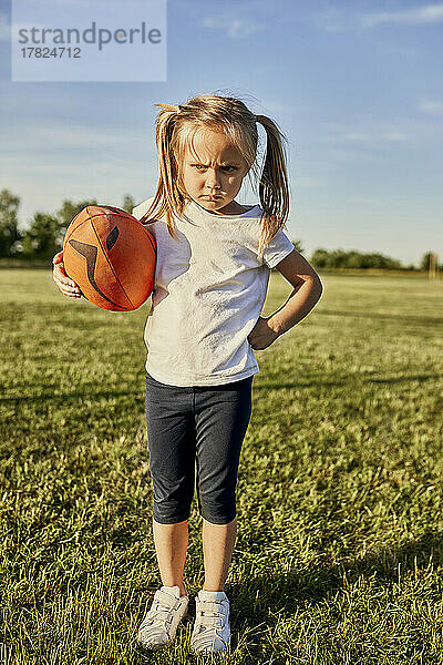 Wütendes blondes Mädchen mit Rugbyball steht an einem sonnigen Tag auf dem Sportplatz