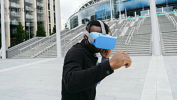 Mann steht in Kampfhaltung und trägt ein Virtual-Reality-Headset vor einem Gebäude