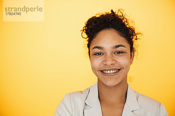 Lächelnde junge Geschäftsfrau vor gelbem Hintergrund
