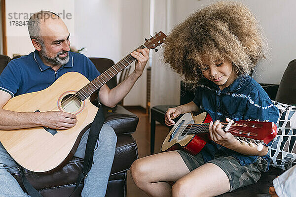 Lächelnder Mann bringt seinem Sohn zu Hause das Gitarrenspielen bei