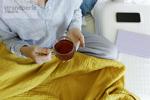 Frau hält eine Tasse Tee und sitzt auf dem Bett