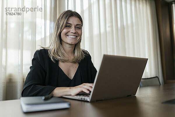 Lächelnde Geschäftsfrau benutzt Laptop auf Tisch im Hotel