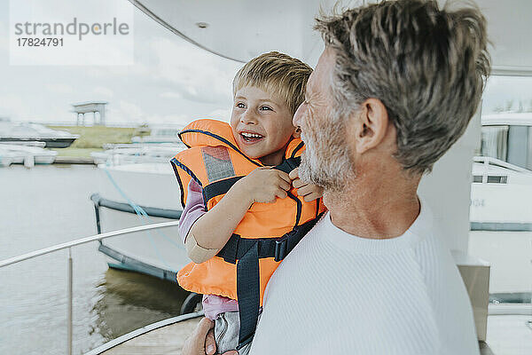 Glücklicher Vater trägt Sohn auf Balkon am Hausboot