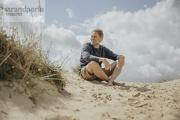 Glücklicher reifer Mann sitzt auf Sand am Strand