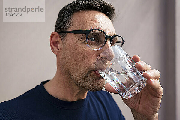 Geschäftsmann mit Brille trinkt Wasser im Glas