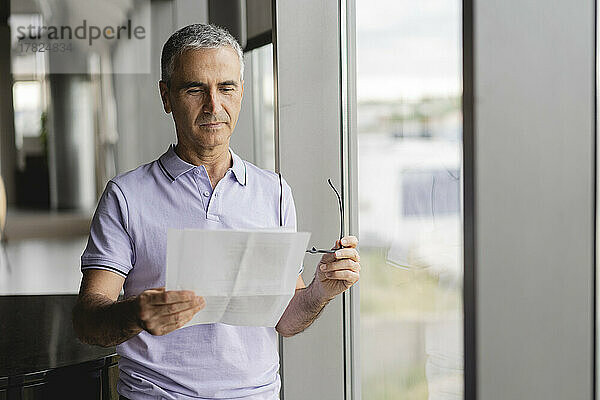 Geschäftsmann überprüft Dokument  das am Fenster im Büro steht
