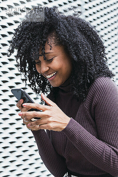 Glückliche Frau schreibt Textnachrichten per Smartphone vor der Wand