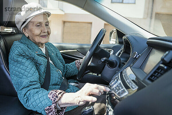 Smiling senior woman playing music on car stereo