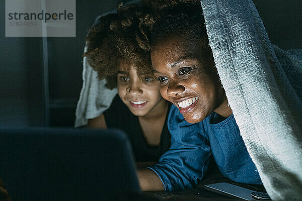 Glückliche Mutter teilt Tablet-PC mit Tochter unter Decke zu Hause