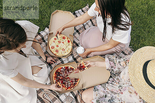 Frauen mit Pizza sitzen auf Picknickdecke im Park