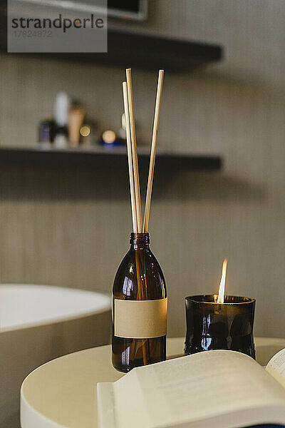 Incense sticks by burning scented candle on table in bathroom