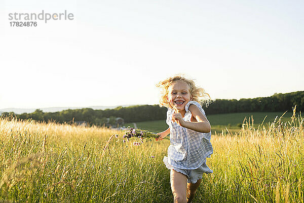 Fröhliches Mädchen läuft an einem sonnigen Tag im Feld