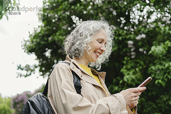 Glückliche Frau  die im Park ihr Mobiltelefon benutzt
