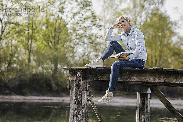 Nachdenkliche Frau sitzt mit Buch am Pier