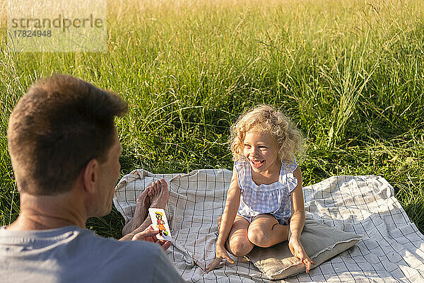 Vater spielt Karte mit fröhlicher Tochter  die auf einer Picknickdecke sitzt