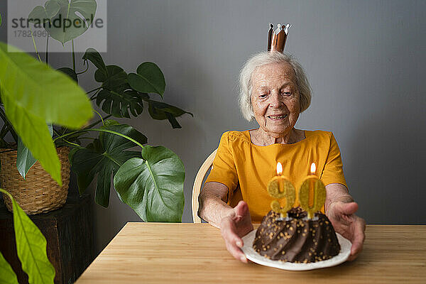 Lächelnde ältere Frau  die zu Hause Geburtstag mit Kuchen feiert