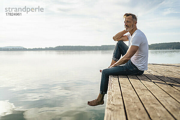 Nachdenklicher reifer Mann sitzt am Rande des Piers am See