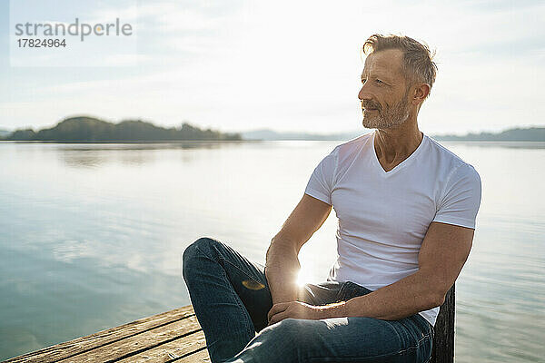 Lächelnder reifer Mann sitzt an einem sonnigen Tag am See