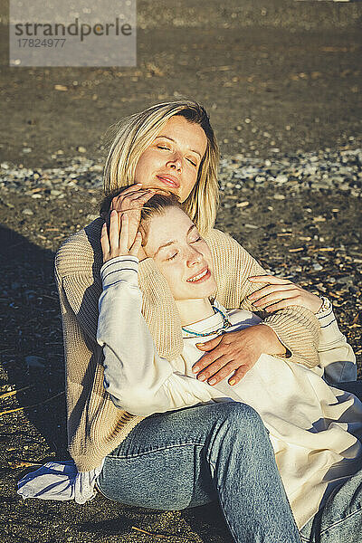 Lächelnde Mutter und Tochter genießen mit geschlossenen Augen den sonnigen Tag