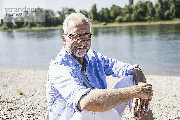 Lächelnder älterer Mann mit Brille am Flussufer an einem sonnigen Tag