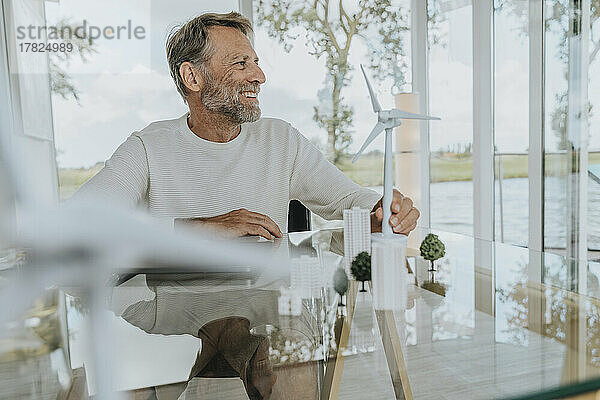Glücklicher reifer Mann mit Windturbinenmodell  der zu Hause sitzt