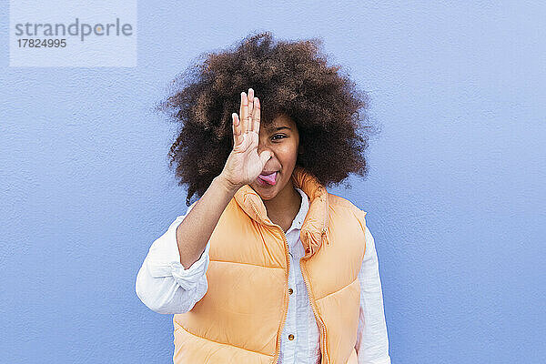 Girl with Afro hairstyle making funny face against blue background
