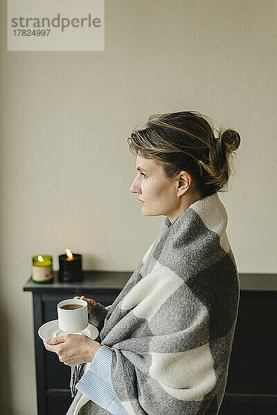 Woman wrapped in blanket having coffee at home
