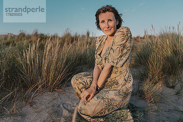 Lächelnde Frau kniet neben Pflanzen am Strand