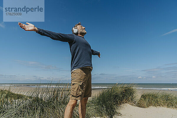 Happy man with arms outstretched standing at beach