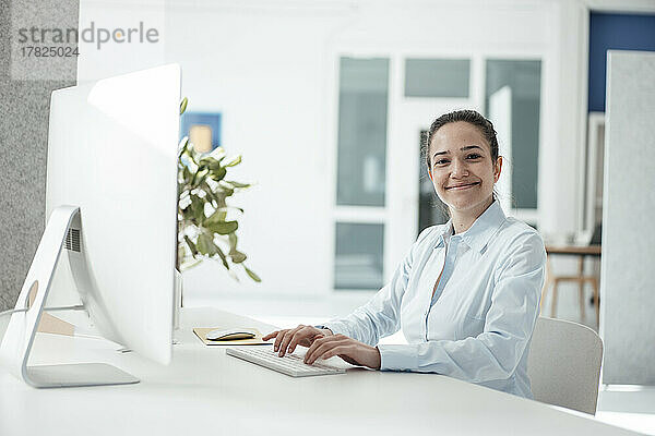 Glückliche Geschäftsfrau mit Computer auf dem Schreibtisch im Büro