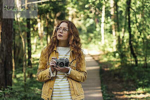 Nachdenkliche Frau hält Kamera im Wald