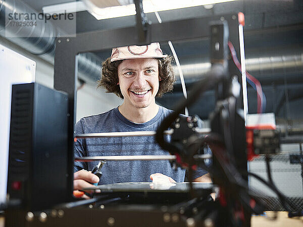 Lächelnder Ingenieur blickt in der Werkstatt auf den 3D-Drucker