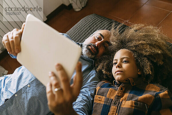Father sharing tablet PC with son lying on bed at home