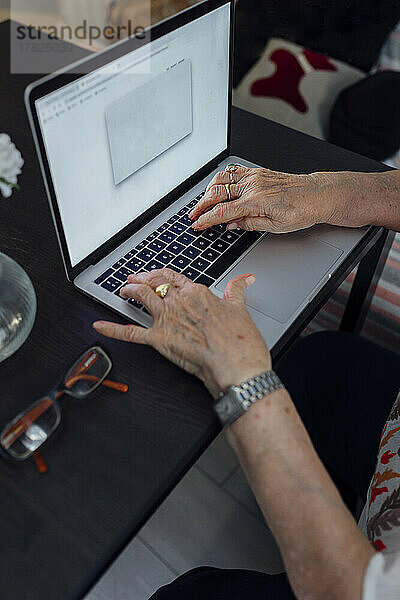 Hände einer älteren Frau  die zu Hause einen Laptop benutzt