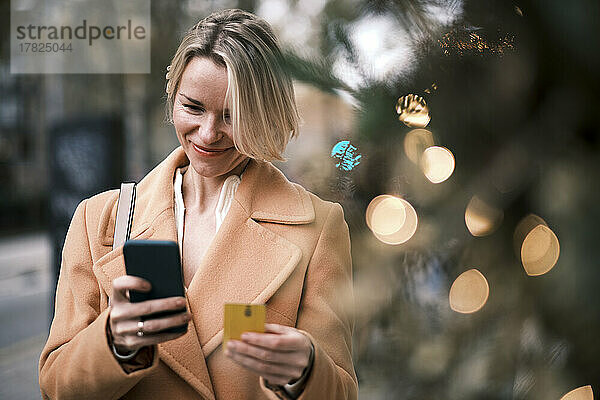 Lächelnde Frau nutzt Kreditkarte  um per Smartphone zu bezahlen