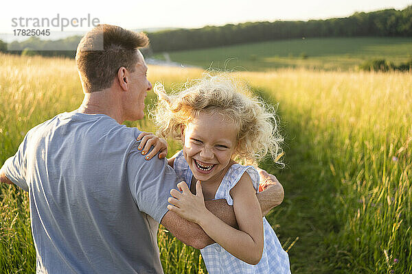 Verspieltes blondes Mädchen genießt es mit seinem Vater auf dem Feld