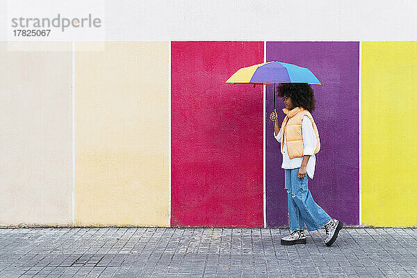 Mädchen läuft mit buntem Regenschirm auf Fußweg