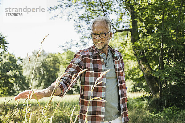 Lächelnder älterer Mann mit Brille  der Pflanzen berührt