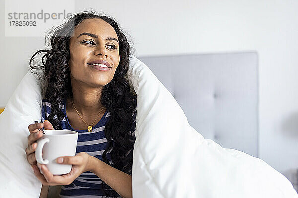 Nachdenkliche Frau genießt Kaffee unter einer Decke