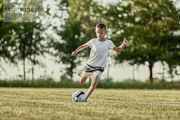 Junge kickt an einem sonnigen Tag Fußball auf dem Sportplatz
